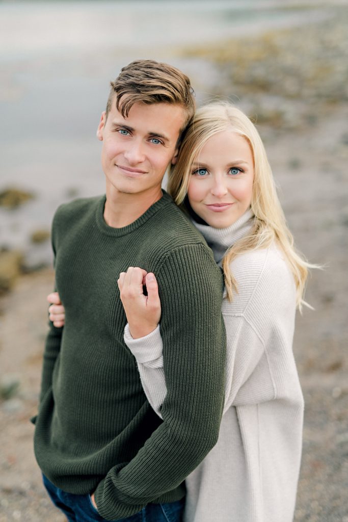gorgeous couple wearing sweaters hugging on the beach