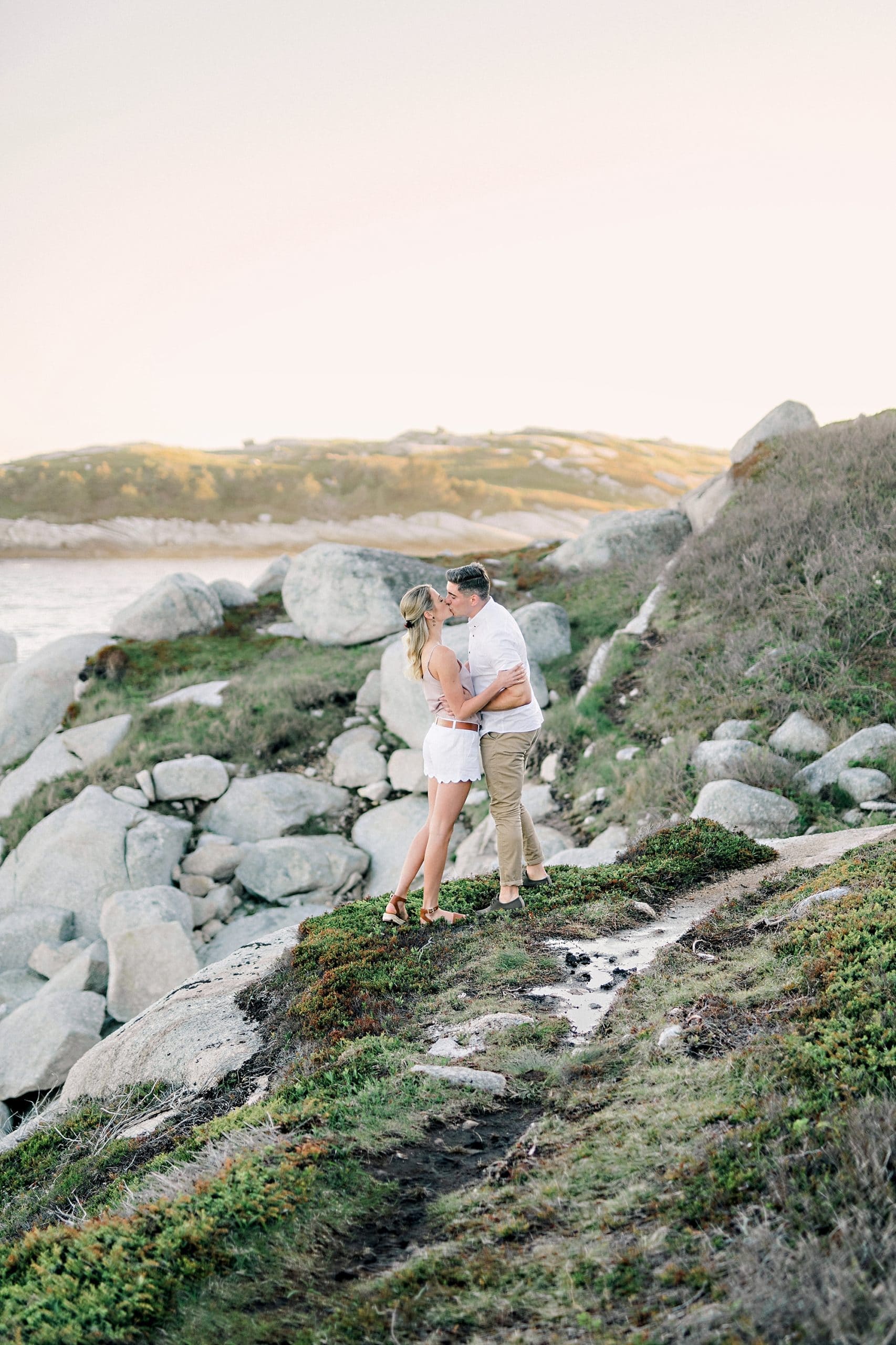 couple kissing on a cliff by the ocean with pink sky and beautiful water views