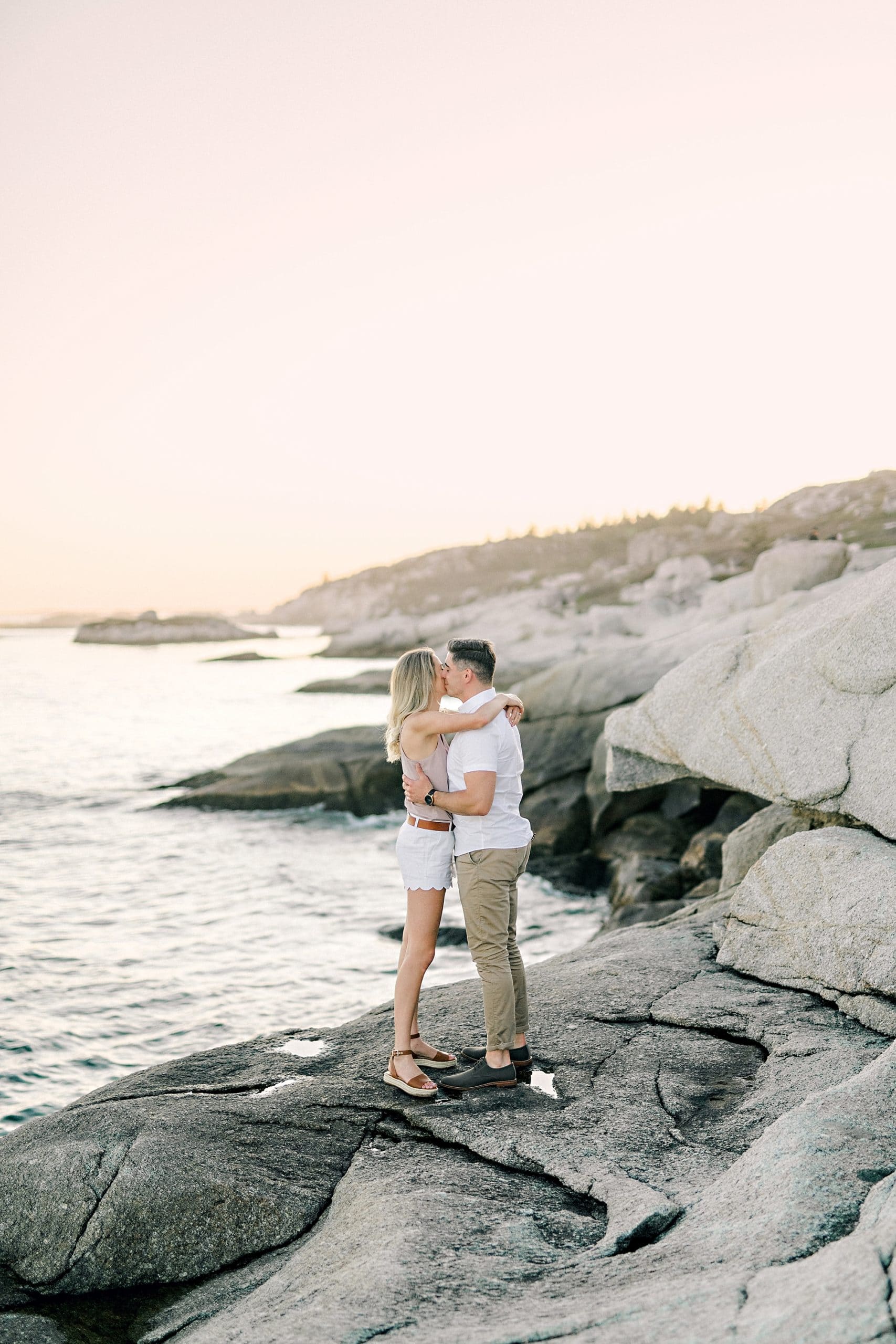 couple embracing on the rocks overlooking the sunset