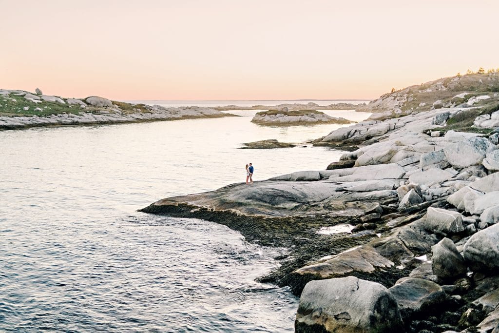 couple embracing on the rocks overlooking the sunset