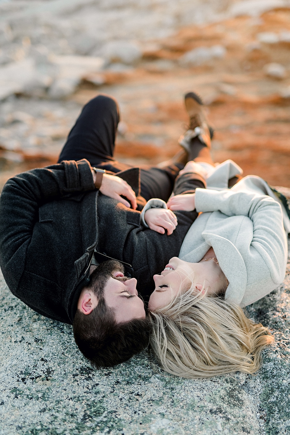 couple laying on rocky cliffs by the ocean at sunset