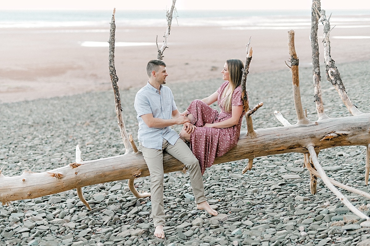 engaged couple sitting on a piece of driftwood that fell down on the beach at sunset 