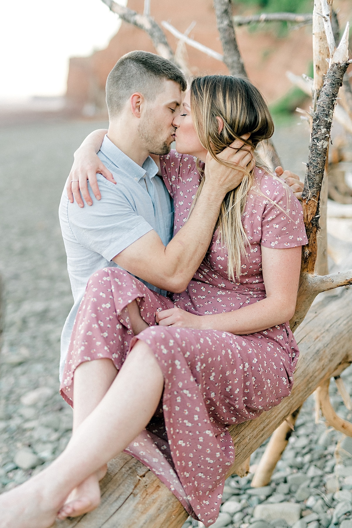 engaged couple kissing on an old log at the beach