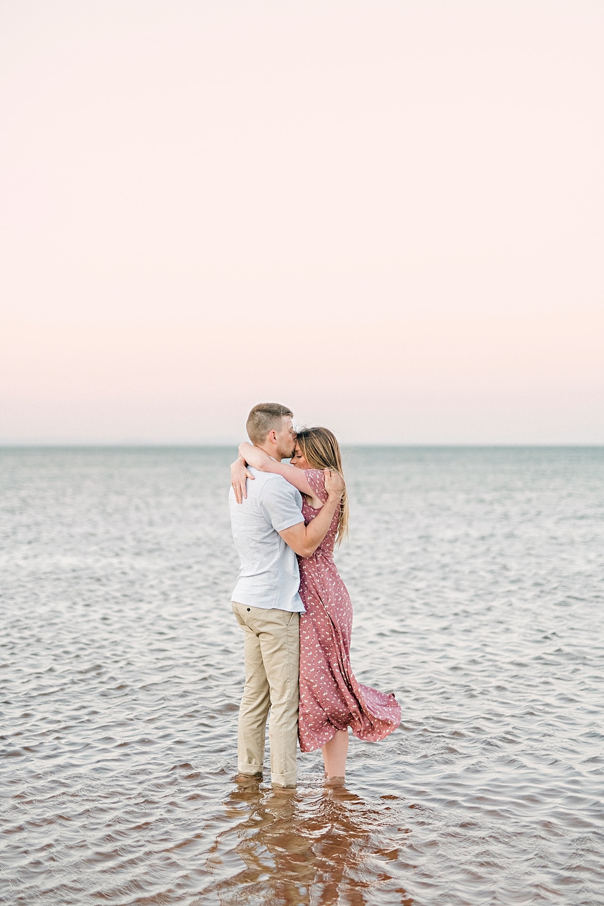 couple kissing in the ocean with pink sky