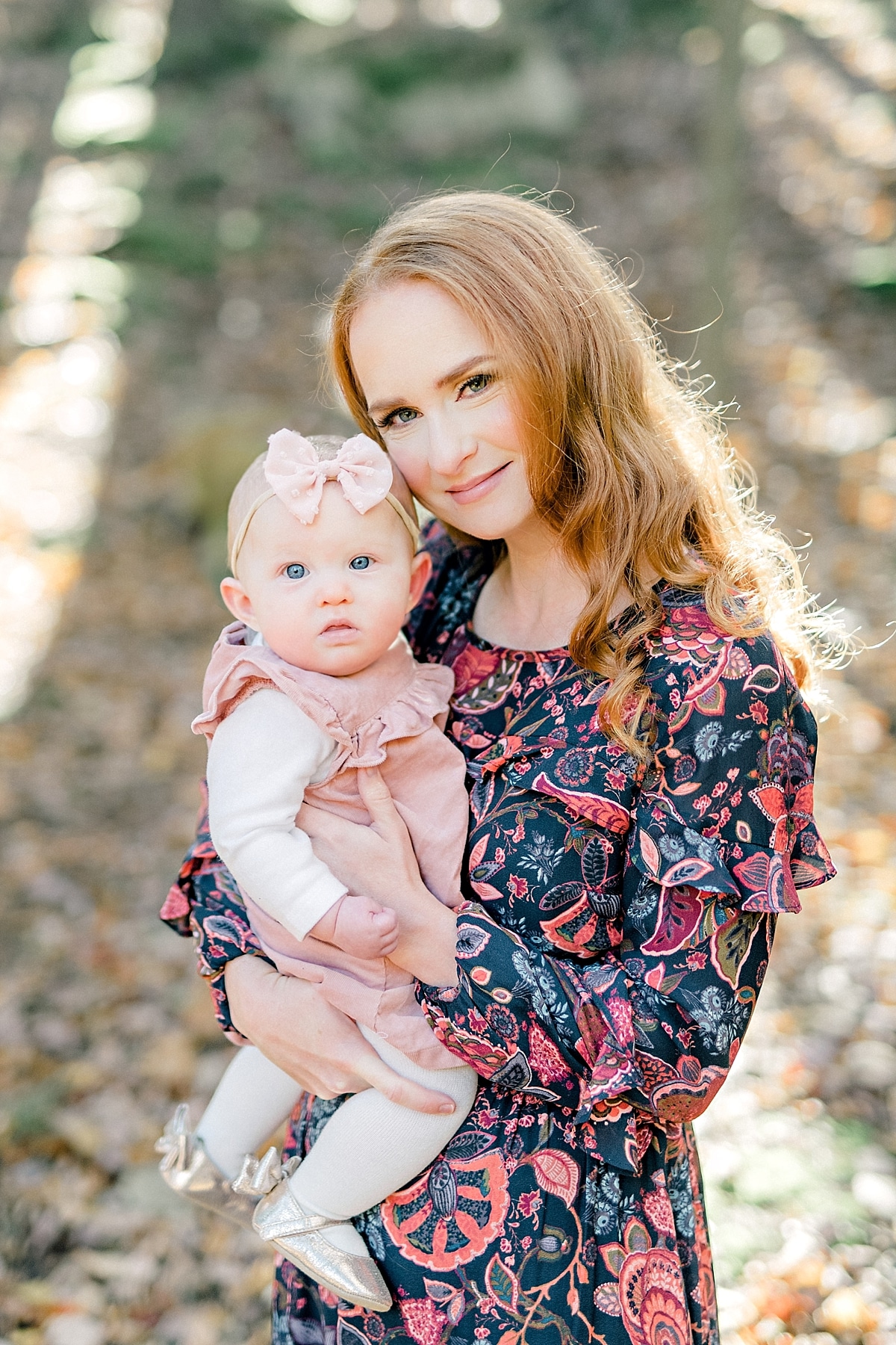 mother with long red hair holds baby girl and smiles during portrait session in the fall time