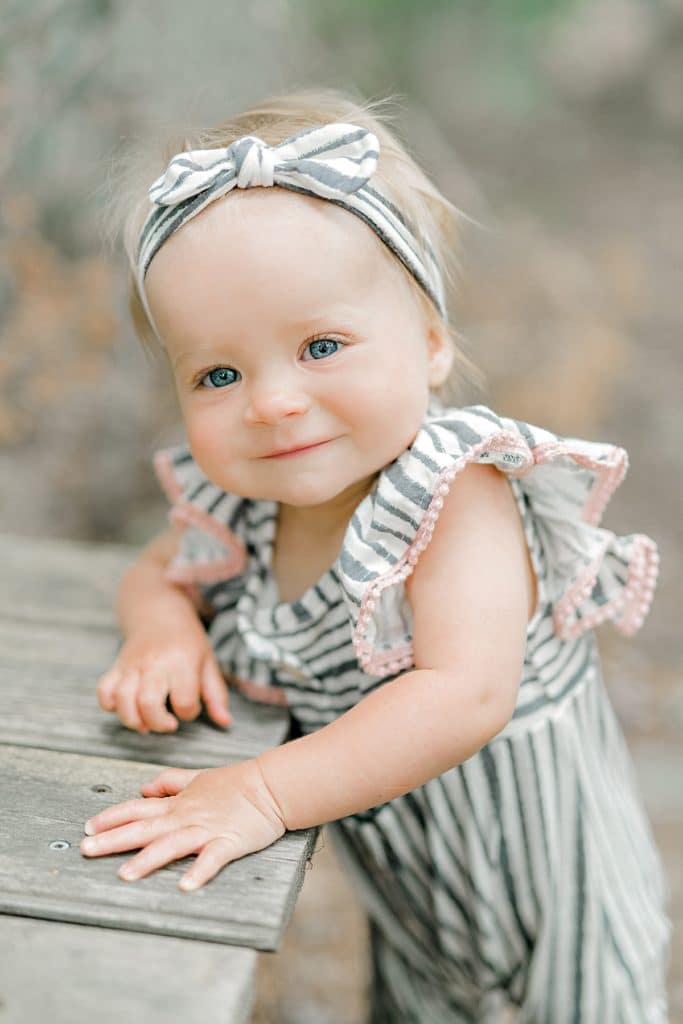 one year old baby in ruffled jumpsuit standing and smiling