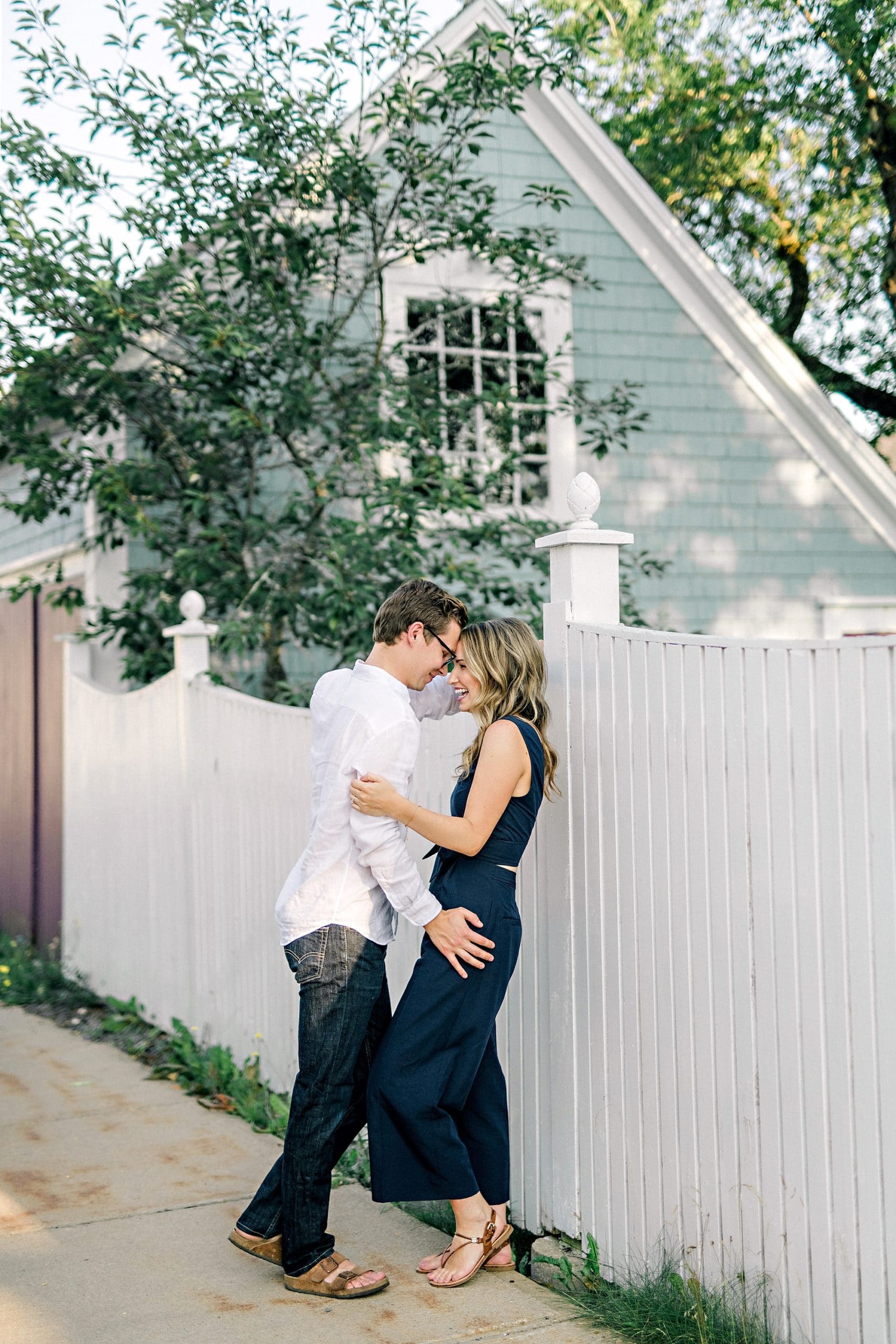 couple in quaint seaside village embracing against white picket fence