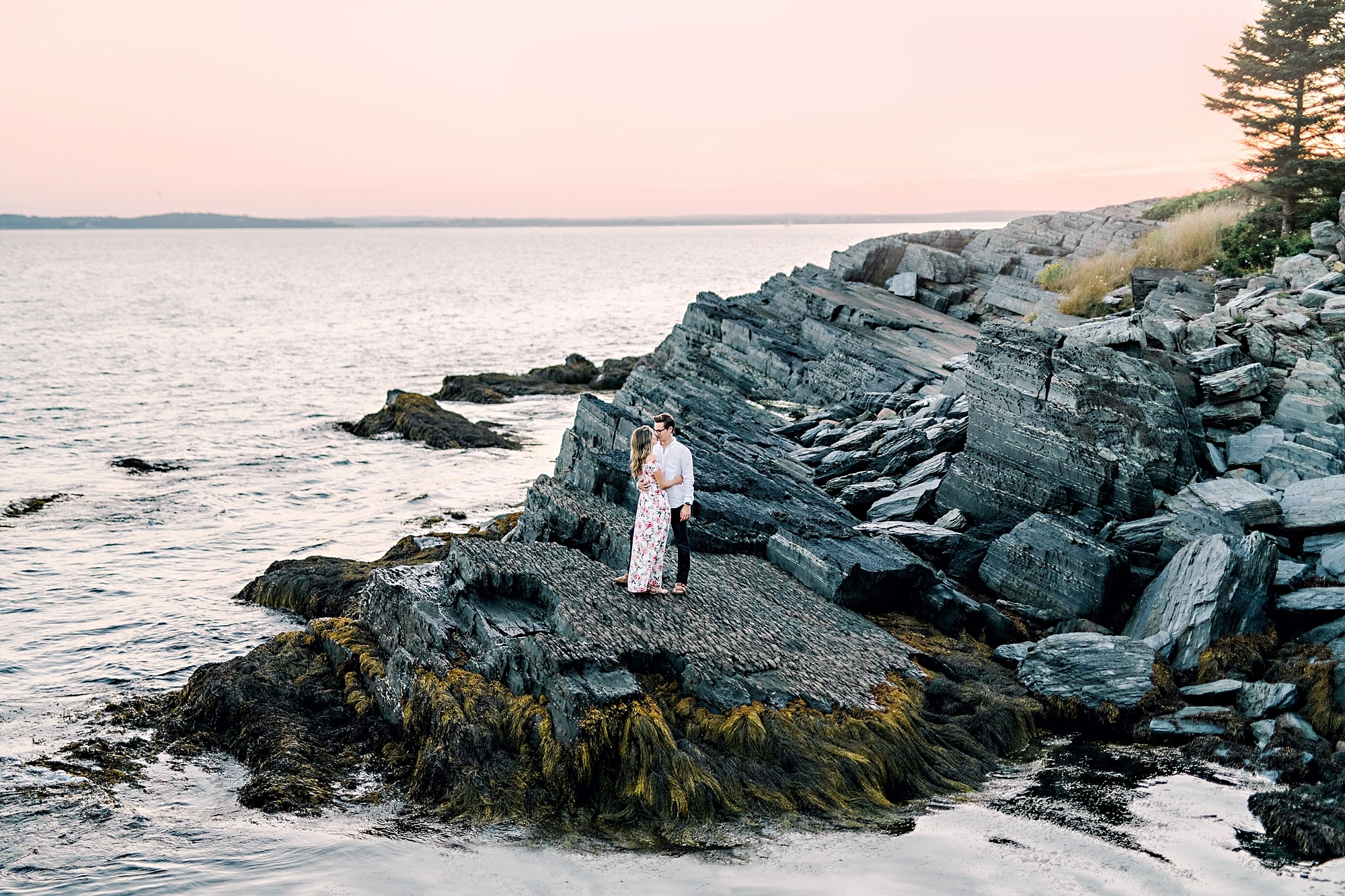 couple standing on blue rocks with pink sky behind them